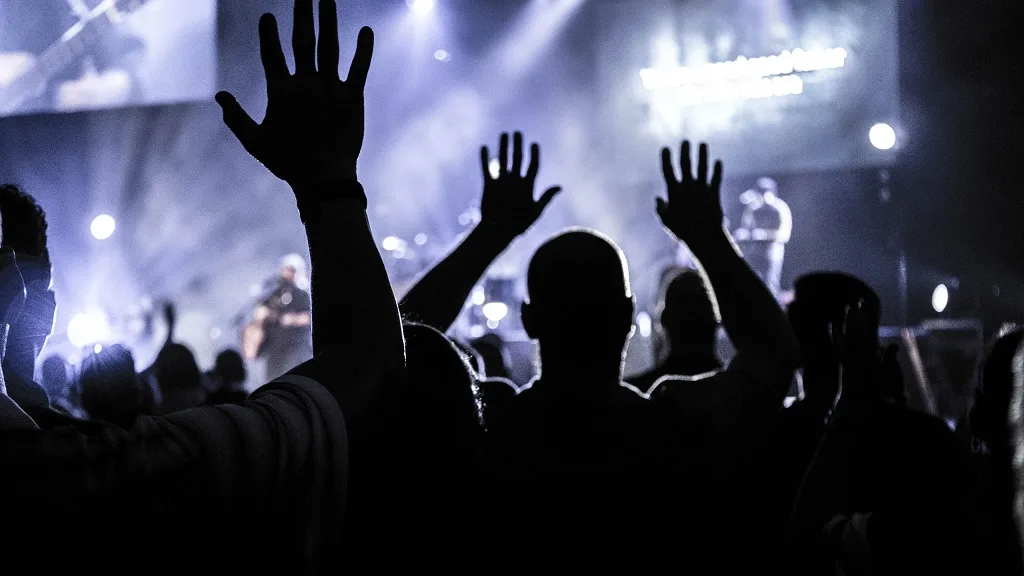 Live event crowd with hands raised, stage lighting behind